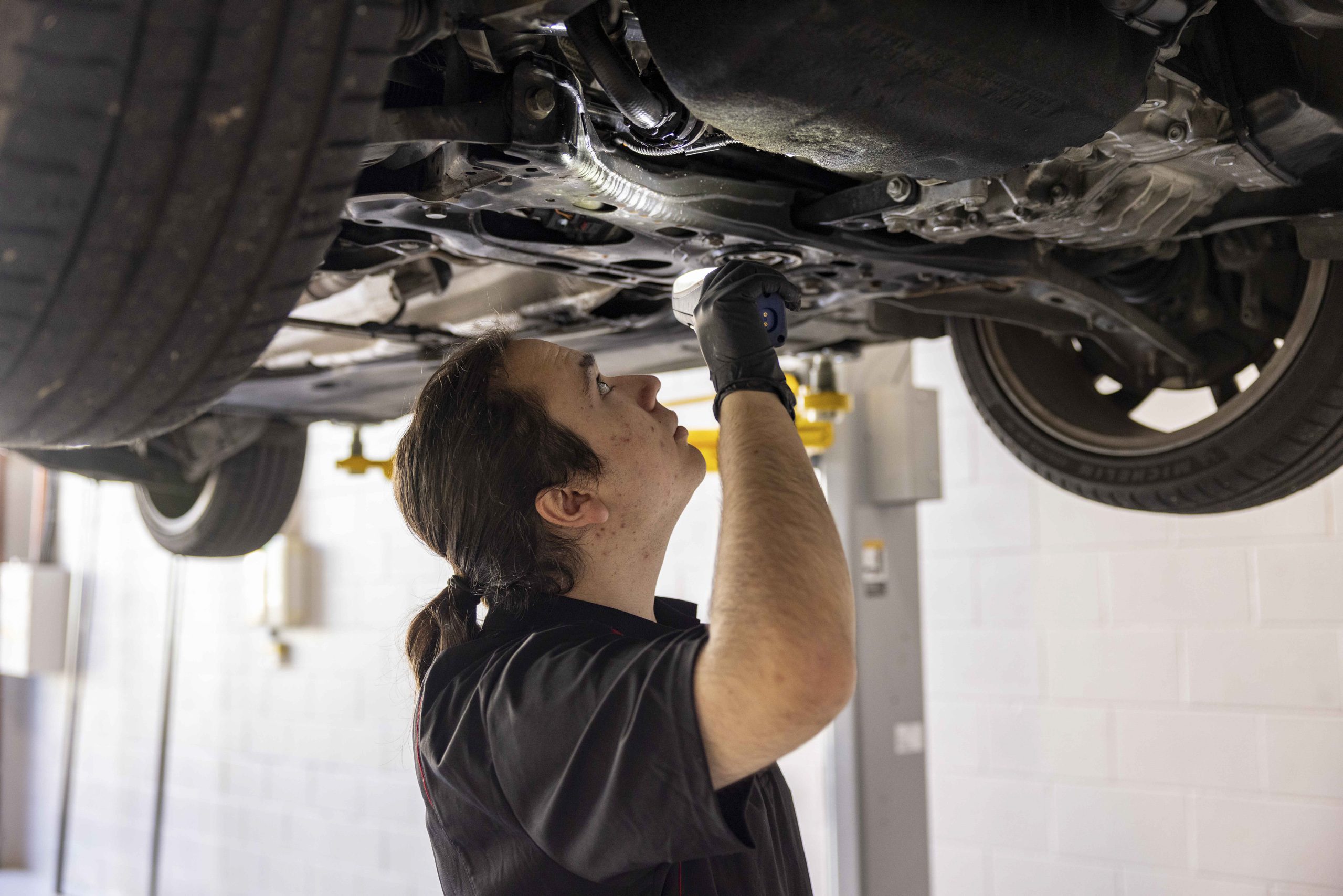 Technician checking suspension and underbody components on a raised car